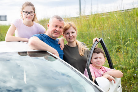 Happy family of four posing next to purchased carの写真素材
