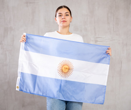 Joyous young woman holding Argentina flag against unicoloured backgroundの写真素材
