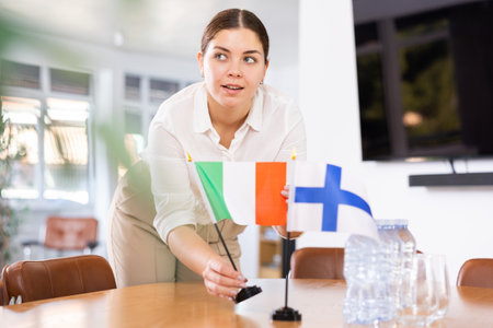 Positive young woman putting flag of Italy on the table with flag of Finland in conference roomの写真素材