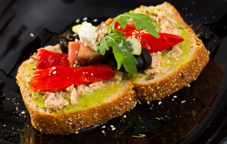 Sandwich with guacamole, canned tuna, feta, vegetables on black plateの写真素材