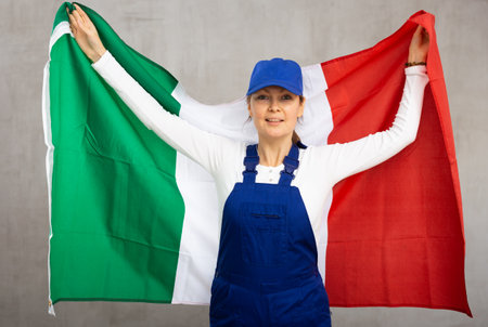 Cheerful female worker with wide grin on her face holding flag of italyの写真素材