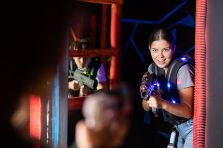 Positive girl holding laser pistol playing laser tag game with friendsの写真素材