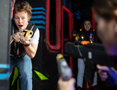 Portrait of positive man with laser gun having fun with her friends on lasertag arenaの写真素材