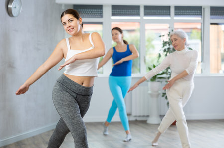 Sporty motivated young elderly women warming up with energetic dances before strength training in...