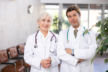 Elderly woman and adult man doctors posing in clinic receptionの写真素材
