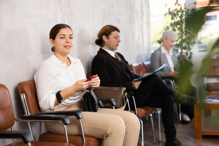 Serious-minded female candidate siting on chair and waiting for job interview in hallwayの写真素材