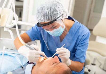 Female dentist drilling tooth to male patientの写真素材