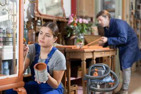 Professional craftswoman restorer in uniform painting cupboard while working in repair shopの写真素材