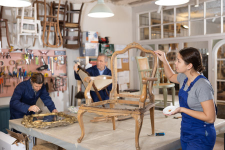 Professional craftswoman restorer in uniform renewing old-fashioned chair while working in repair shopの写真素材