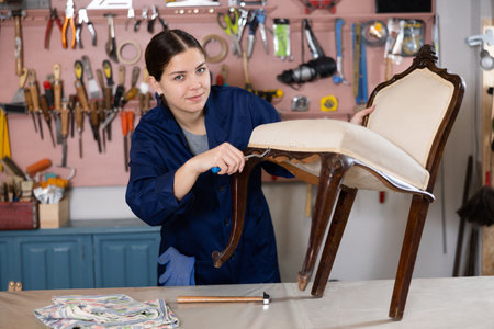Portrait of skillful repair woman carpenter renovating chair furniture using tools in woodwork studioの写真素材