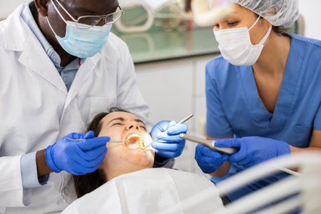 Dentist and nurse performing tooth enamel restoration operation on womanの写真素材