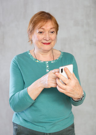Positive interested aged woman looking at mobile phoneの写真素材