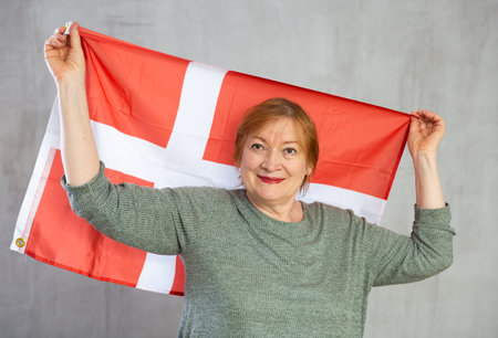 Smiling elderly woman waving flag of Denmark in studioの写真素材