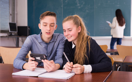 Cheerful teenagers with phone in schoolroomの写真素材