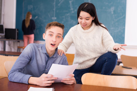 Delighted teenager and Chinese girl schoolmate reading notificationの写真素材