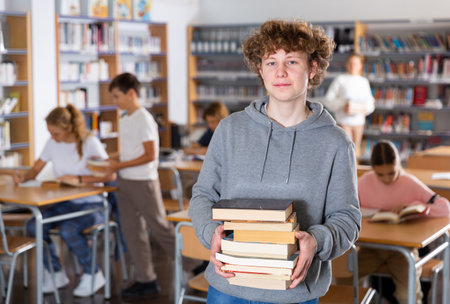 Teenager boy standing with a stack of books in libraryの写真素材