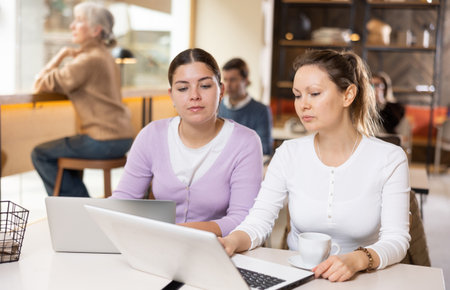 Two confident female cafe customers enjoying coffee while working on laptopの写真素材