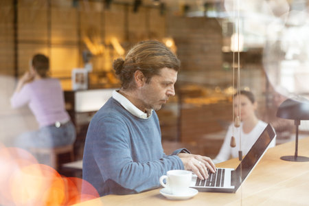 Positive man spending time in coffeehouse with laptop and coffeeの写真素材