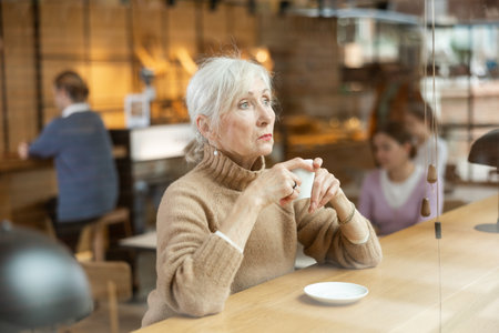 Calm mature woman enjoying peace and quiet alone in cozy cafeの写真素材