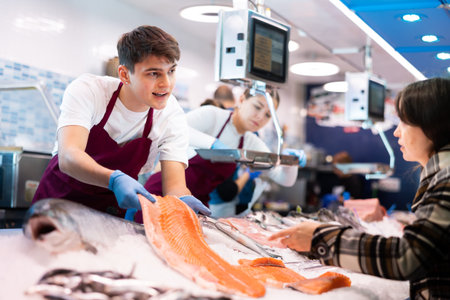 Responsive salesman demonstrating piece of salmon in fish storeの写真素材