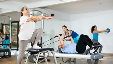 Aged woman practicing pilates on pedal fitness chair in sports hallの写真素材