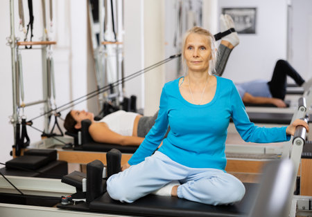 Senior female performing mermaid exercise on reformer Pilates machine for improving and maintaining mobility in gymの写真素材