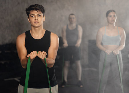 Young guy doing exercises with elastic loop band in gymの写真素材
