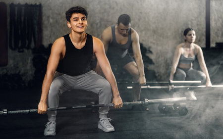 Smiling sporty guy performing deadlift with barbell in gymの写真素材