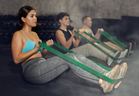 Focused young woman training with resistance band for health wellness, strong biceps or abs muscles in gym health centerの写真素材