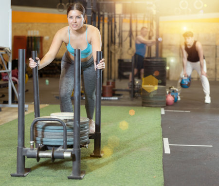 Motivated young woman performing heavy sled push in gymの写真素材