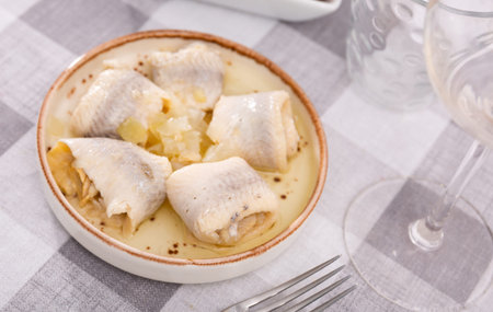 on checkered tablecloth plate with appetizer - rolls of salted Atlantic herring fillet with onions