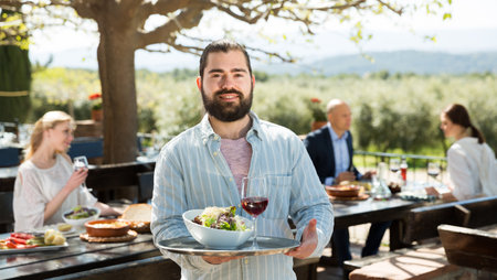 Adult beard waiter who is standing with order at country outdoor restaurantの写真素材