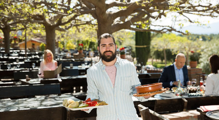 Adult beard waiter who is standing with order at country outdoor restaurantの写真素材