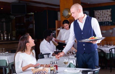 Polite waiter serving young female guest of restaurantの写真素材