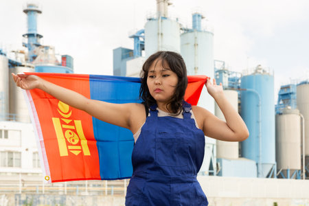 Sad young woman with flag of Mongolia against background of factoryの写真素材