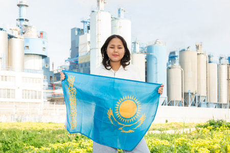 Happy asian girl with flag of kazakhstan standing in front of industrial sceneryの写真素材