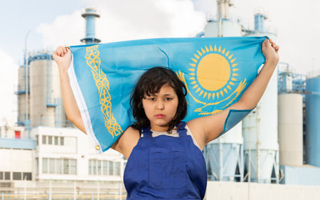 Sad young woman with flag of Kazakhstan against background of factoryの写真素材