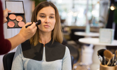 Hands of makeup artist applying powder brush on female client faceの写真素材