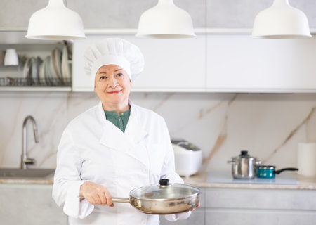 Adult woman in cook uniform posing with frying panの写真素材