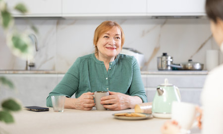 Smiling adult woman and young woman drinking tea in kitchenの写真素材