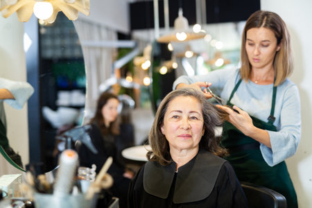 Elderly woman getting haircut by professional female hairdresserの写真素材