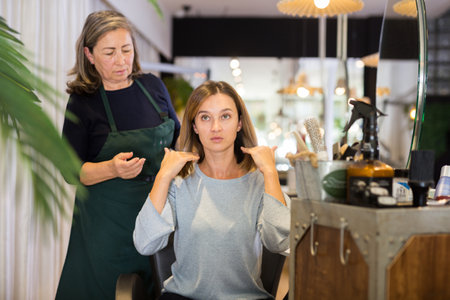 Aged female hairdresser offering modern hairstyling to young womanの写真素材