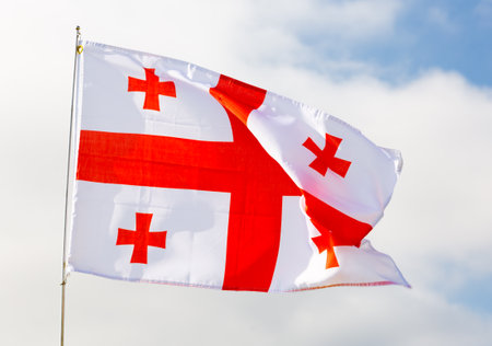Against background of cloudy sky,white-red flag of Georgia flutters on flagpoleの写真素材