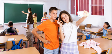 Two cheerful schoolgirls take a selfie during recess in classroom