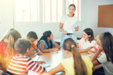 Female teacher conducting lesson with preteen children sitting around deskの写真素材