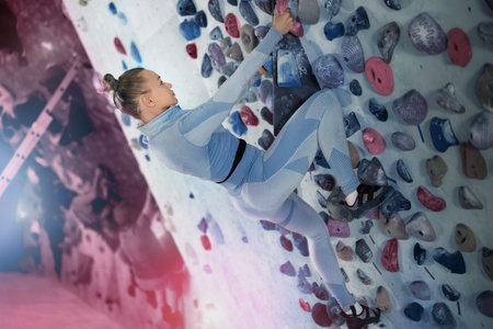 Concentrated woman moving up bouldering wall in climbing gym