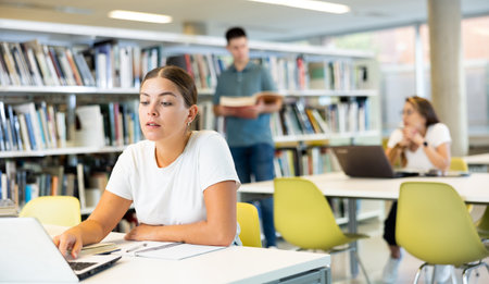 Positive young lady working remotely using a computer in a quiet libraryの写真素材
