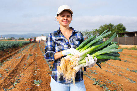 Smiling woman agriculturist with leek on vegetable plantationの写真素材