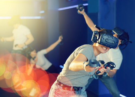 Young woman in VR glasses playing virtual game with handheld controllers