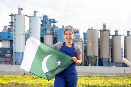 Happy young woman worker with flag of Pakistan against background of factoryの写真素材